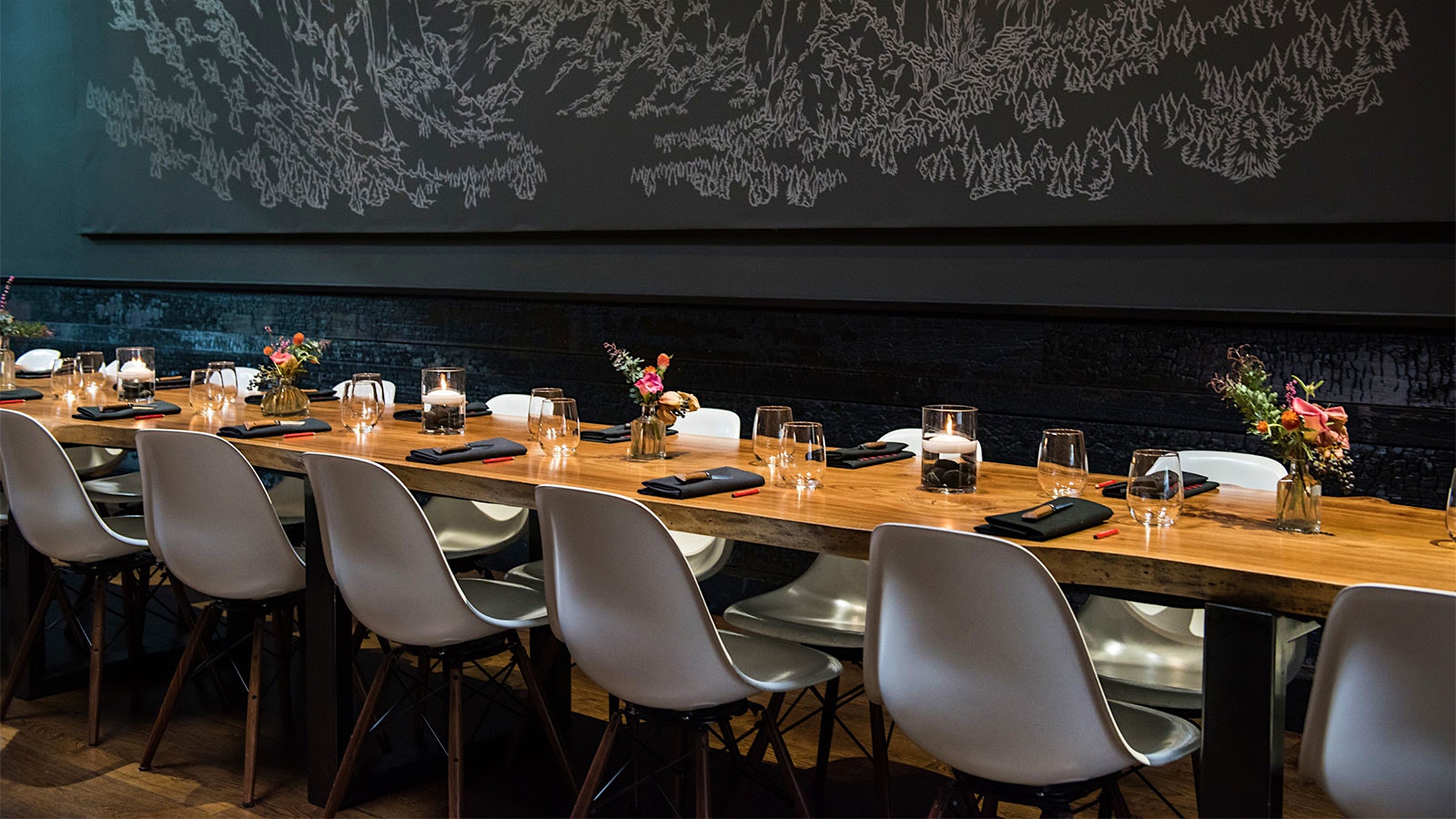 A long, narrow communal table at Lazy Bear with a large artwork on the wall behind it
